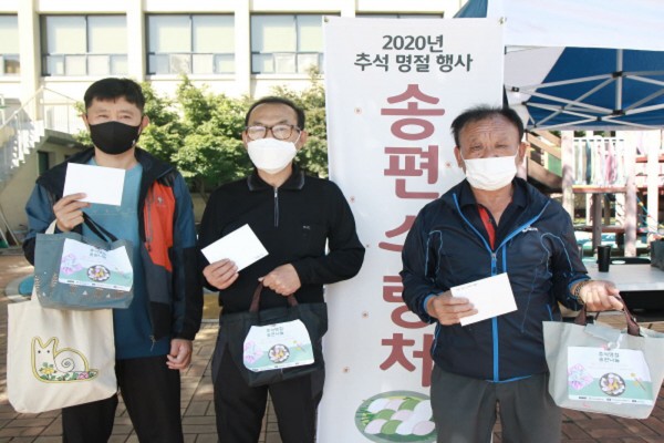 추석 명절 행사 송편 수령처 현수막 앞에 이용자 세 사람이 송편 키트와 손편지를 들고 서있다.